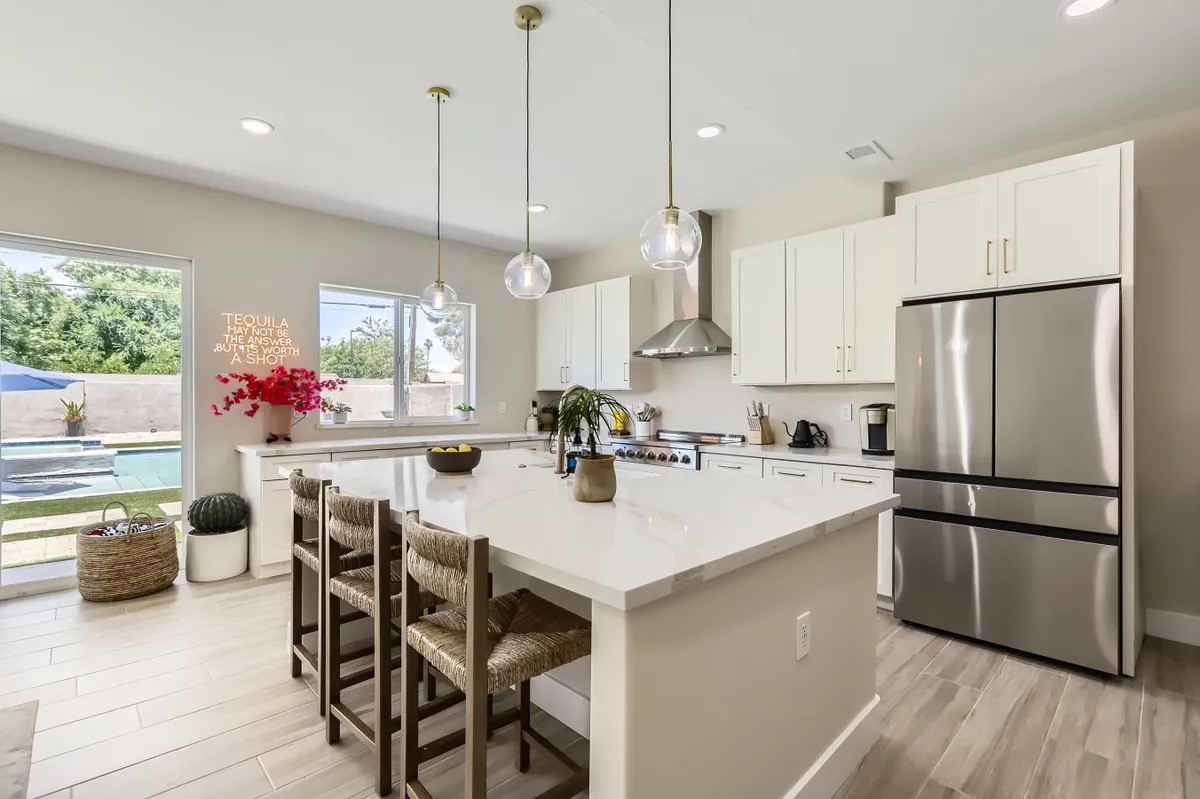 This image showcases a bright, welcoming kitchen with an island countertop, bar stools, modern appliances, and large windows that frame relaxing exterior views. The open layout is perfect for both cooking and entertaining, with plenty of space for social interactions.