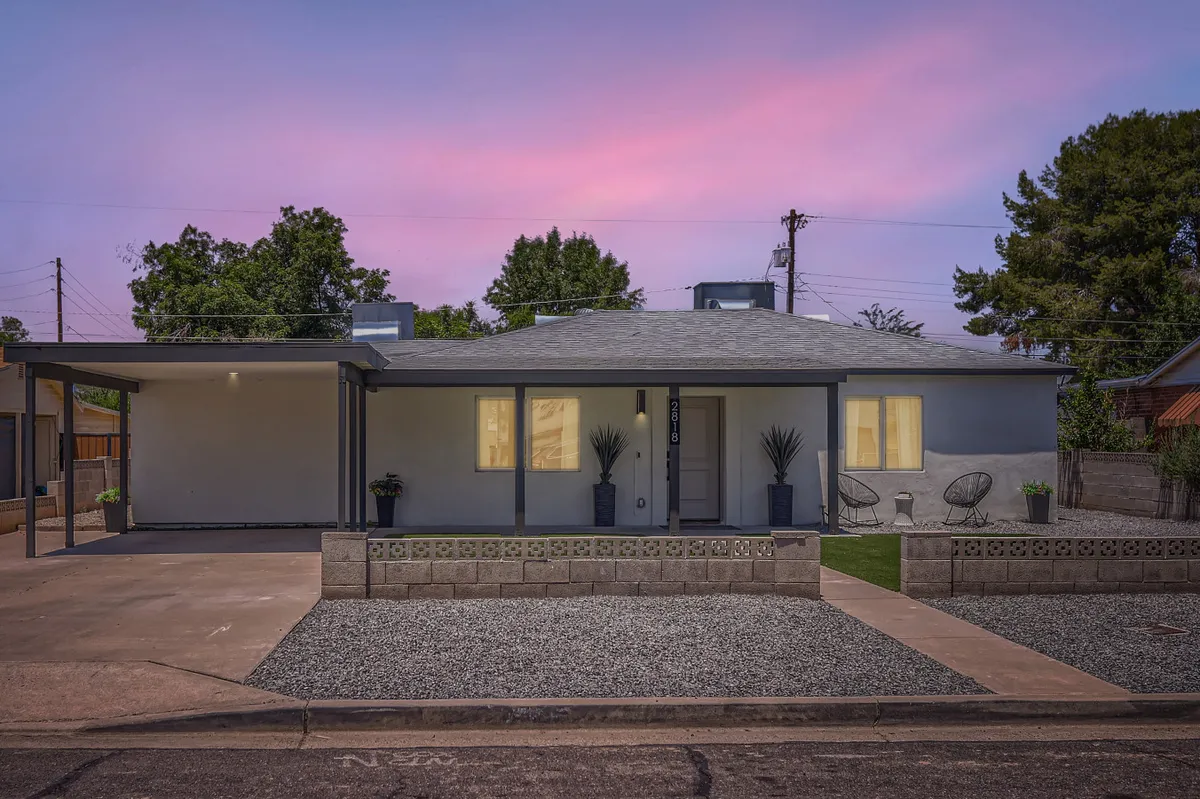 A charming front porch with gravel landscaping, potted plants, a decorative block wall, and a cozy sitting area. The scene suggests a tranquil retreat for morning coffee or enjoying the sunset, highlighting the welcoming entry to the home.