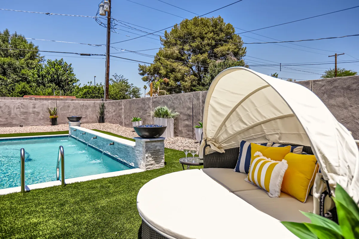 This image features a tranquil swimming pool surrounded by lounge chairs and decorative planters, with sunset lighting and spaces for sunbathing or peaceful outdoor relaxation. The mood is serene, inviting guests to unwind in a resort-like backyard setting.