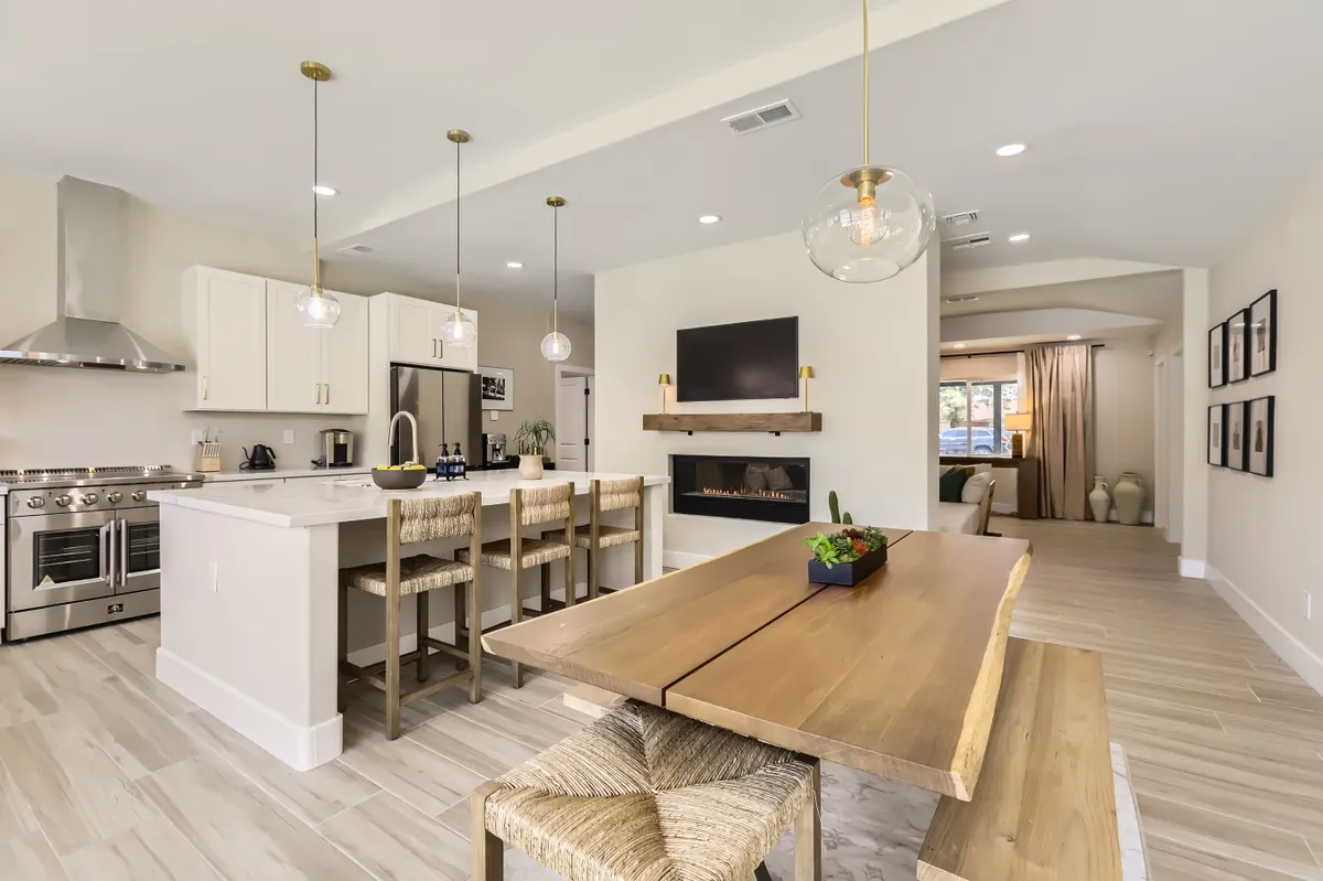 A warm and inviting perspective of the kitchen and dining area, featuring a spacious kitchen island, adjacent dining table, fireplace, and television. The open concept layout promotes seamless movement and conversation between cooking and dining spaces.
