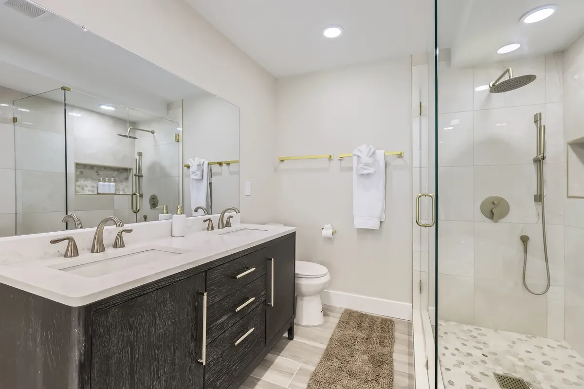 A contemporary bathroom featuring a double vanity, glass shower, and mirrored wall, designed for comfort and relaxation. The layout and fixtures evoke a spa-like atmosphere ideal for unwinding after a long day.