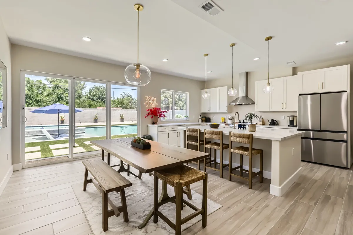 A bright, airy open-plan space featuring a dining table, kitchen island, and expansive windows offering a view of the pool. The layout encourages conversation and movement, perfect for entertaining guests or casual gatherings.