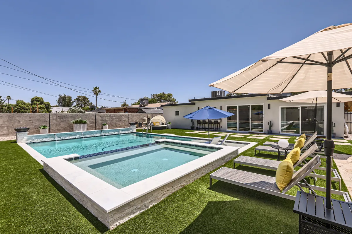 This inviting exterior image showcases the backyard swimming pool as the focal point, surrounded by comfortable lounge chairs and umbrellas set in a landscaped garden. The tranquil scene hints at leisurely swims, sunbathing, and peaceful relaxation, all in a private and serene backyard setting.