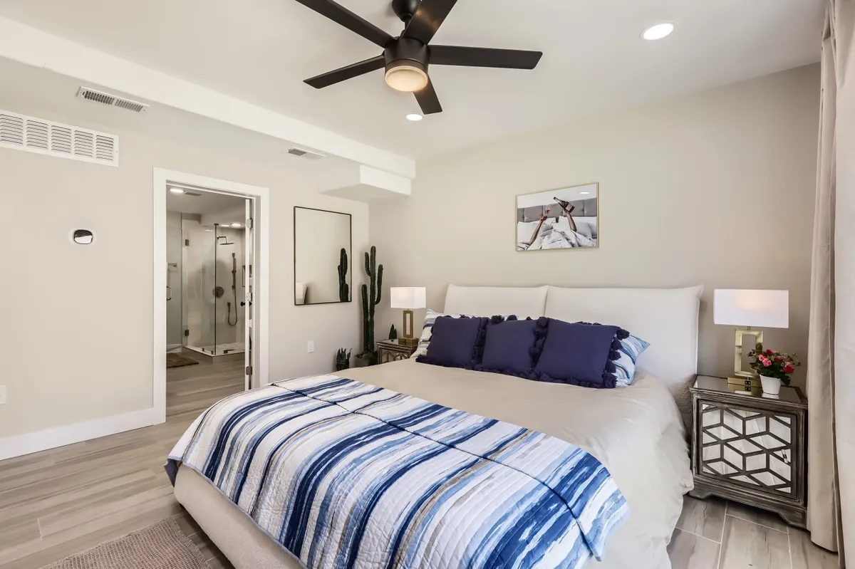 A calm bedroom with a comfortable bed adorned with decorative pillows, flanked by nightstands, cactus plants, and complementary artwork. The soft light and uncluttered decor emphasize a serene and restful ambiance.