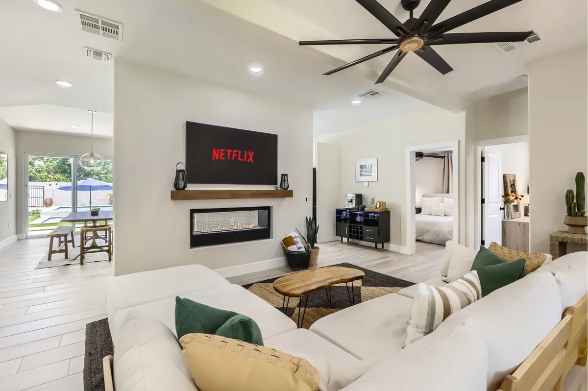 A stylish living room with a plush sofa facing a built-in fireplace and a wall-mounted screen displaying Netflix. The space features a coffee table, contemporary decor, and atmospheric lighting conducive to entertaining or relaxing movie nights.
